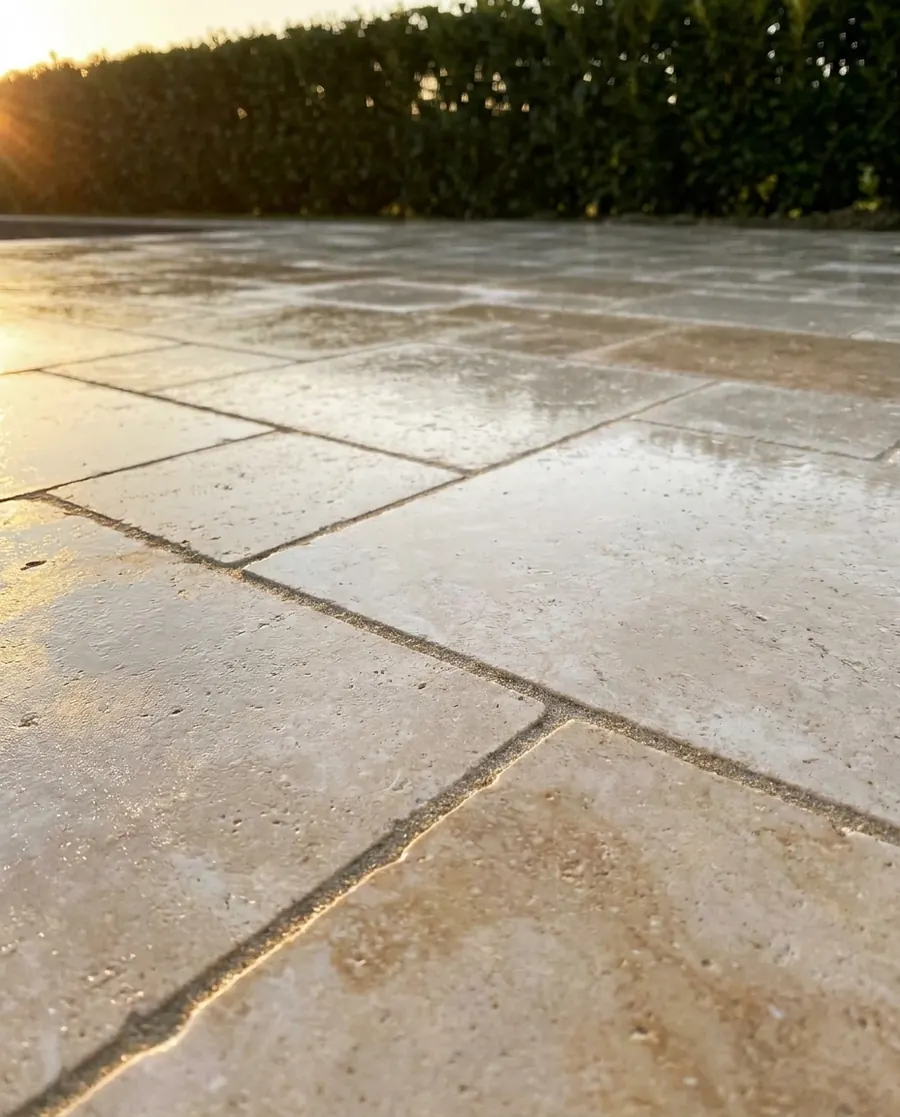 Freshly sealed cream and tan pavers with a satin sheen and crisp sand joints, photographed low at golden hour with a hedge behind